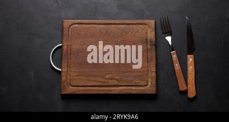 Fork and knife with wooden handle and cutting board on black background, top view Stock Photo