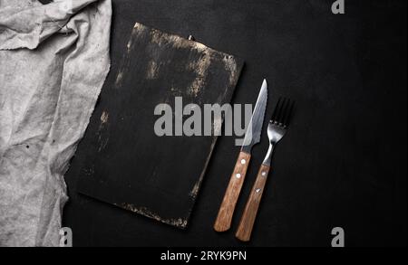 Fork and knife with wooden handle and cutting board on black background Stock Photo
