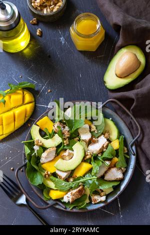 Healthy diet salad with arugula, mango, avocado, chicken grill, walnuts and vinaigrette dressing on a dark stone countertop. Cop Stock Photo