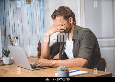 Man clearly overwhelmed and stressed out at work. His head in his hands, covering his face with palm, appearing to be in state o Stock Photo