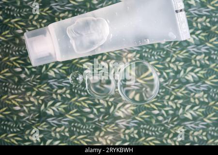 A transparent bottle of cosmetic gel on a green background with drops of the product. Stock Photo