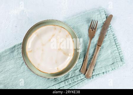An empty plate with a gold rim, with a fork and a knife, with a teal napkin Stock Photo