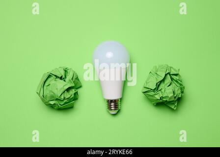 Crumpled green balls of paper and glass white lamp on green background, top view Stock Photo