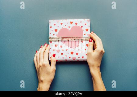 Top view of female hands holding a wrapped gift with a large paper heart. Birthday and Valentine's Day gift. Stock Photo