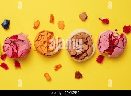 Broken round macarons with crumbs on a yellow background, delicious dessert, top view Stock Photo