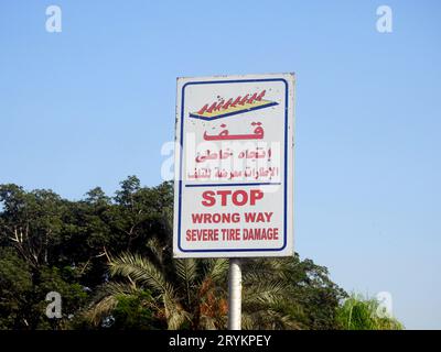 A warning road sign in Arabic and English, Translation of Arabic words ( Stop, Wrong way, Severe Tire Damage ) as a caution before a spikes barrier on Stock Photo