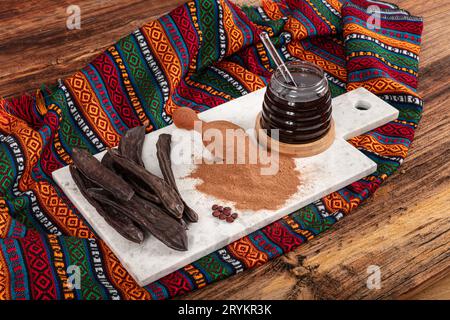 Carob pods and carob beans. Dry carob pods and carob powder over wooden background. Organic healthy ingredient for vegan vegetarian food and drinks, c Stock Photo