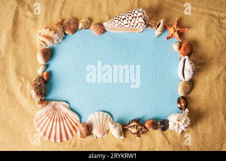 Invitation or greeting card mockup in frame of seashells and starfish on the ocean sandy beach background. Stock Photo
