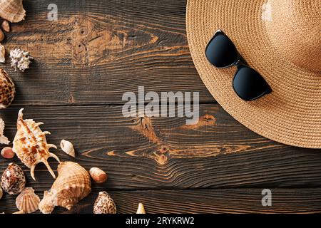 Straw hat, sunglasses and various seashells on dark wooden background with copy space for text Stock Photo