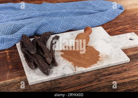 Carob pods and carob beans. Dry carob pods and carob powder over wooden background. Organic healthy ingredient for vegan vegetarian food and drinks, c Stock Photo