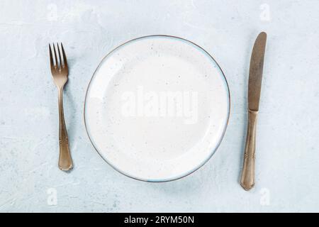 An empty white plate with a blue rim, with a fork and a knife, overhead Stock Photo