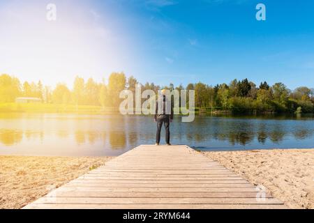Young man standing alone on edge of wooden footbridge and staring at lake Stock Photo
