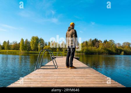 Young man standing alone on wooden bridge and staring at lake Stock Photo