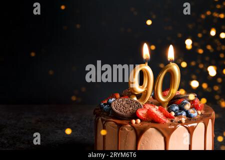 Chocolate birthday cake with berries, cookies and number ninety golden candles on black background, copy space Stock Photo