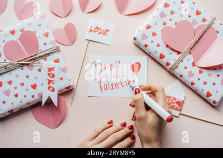 Woman signs a postcard Valentine BE MY VALENTINE. Festive love decor and gifts. Stock Photo