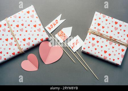 On the gray surface there are gift boxes wrapped in textured paper and props with a love message. Festive romantic decor and Val Stock Photo