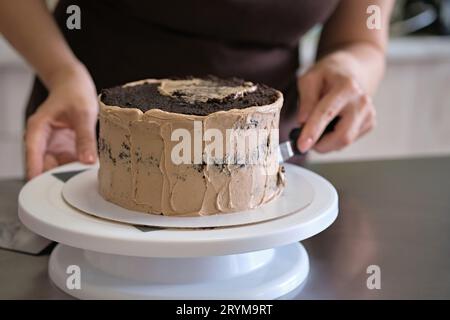 Woman pastry chef making chocolate cake with chocolate cream, close-up. Cake making process, Selective focus Stock Photo