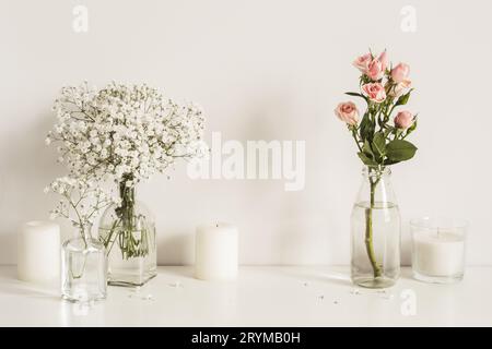 Composition with white and pink flowers in glass bottles and candles on table wall background. Copy space for artwork Stock Photo