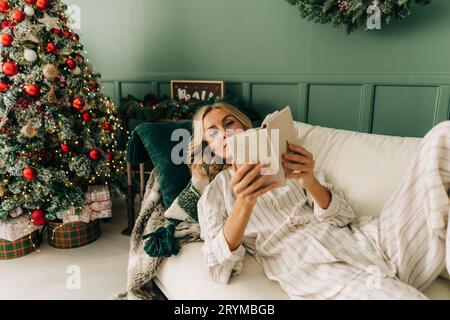 Elegant woman lies on the sofa in the Christmas holidays and is resting and relaxing reading a book. Stock Photo