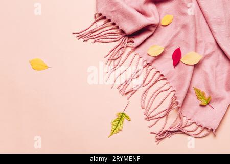 Pink cozy scarf with tassels and scattered leaves on pastel background. Hello autumn concept Stock Photo