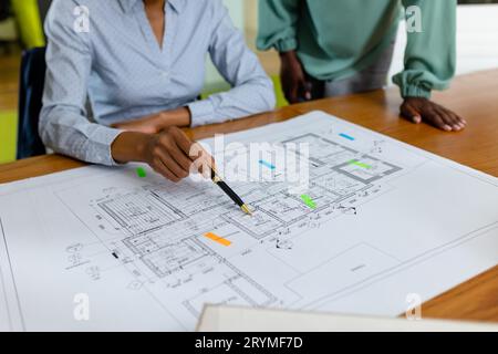 Midsection of african american female architects analyzing blueprint on desk in office, copy space. Unaltered, architecture, construction industry, de Stock Photo