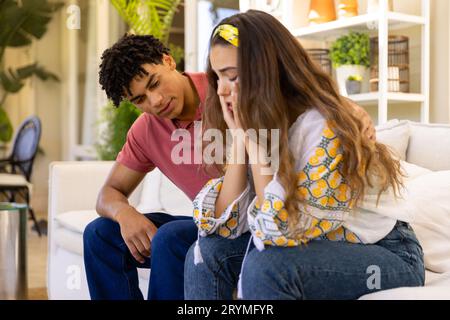 Diverse couple sitting on sofa in living room, man comforting sad woman Stock Photo
