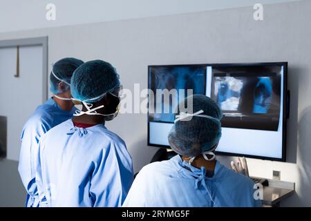 Diverse group of surgeons discussing x rays on screen in operating theatre Stock Photo