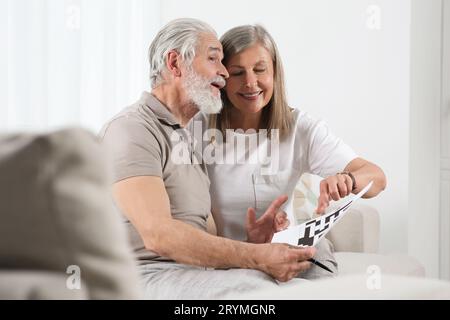 Senior couple solving crossword on sofa at home Stock Photo