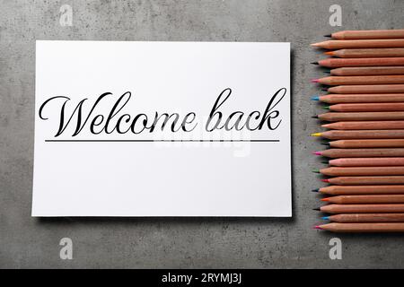 Paper with phrase Welcome Back and pencils on grey table, flat lay Stock Photo