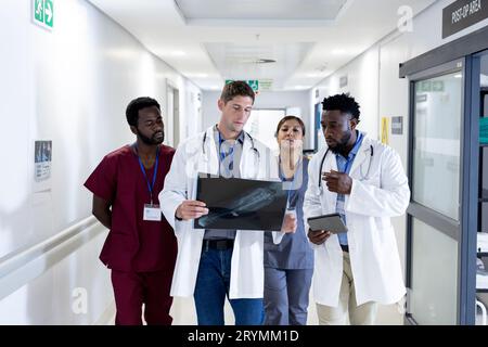 Diverse group of doctors discussing x ray walking in hospital corridor Stock Photo