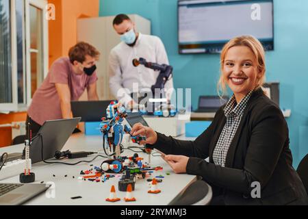 A woman sitting in a laboratory and solving problems and analyzing the robot's verification. In the background, colleagues are t Stock Photo