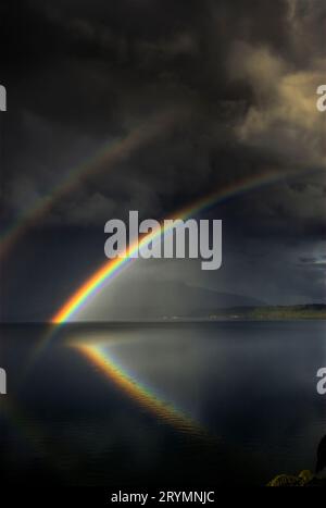 Double rainbow reflected in Lake Tarawera, ahead of approaching storm, Rotorua, New Zealand Stock Photo