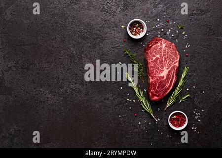 Fresh raw marbled beef rib eye steak, herbs and spices on black stone background, copy space Stock Photo