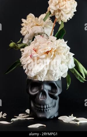 Surreal still life with skull and withering peonies on black background. Halloween or aging concept Stock Photo