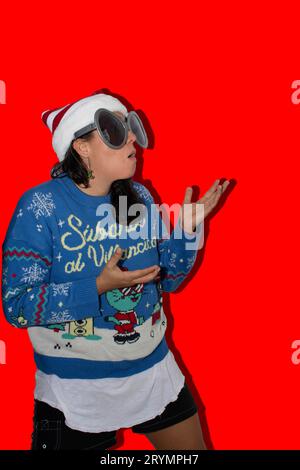 Woman with long hair, making a surprised gesture looking upwards where there is blank space for text. The woman is wearing a blue ugly sweater, a Chri Stock Photo