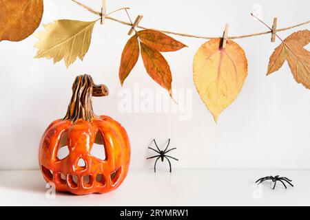Ceramic pumpkin jack lantern and autumn leaves garland on table wall background. Home decoration Stock Photo
