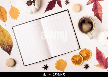 Notepad and cup of coffee on white table with autumn leaves pattern Stock Photo