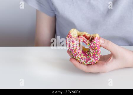 Children's hand stretches bitten donut in pink icing and jam filling Stock Photo