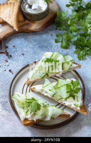 Healthy breakfast or holiday snacks. Toast with cucumbers, herbs and ricotta on a light slate stoleshnitsfone. Stock Photo