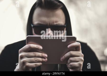 A Man with a tablet computer sits in an open-air park. Young Hacker in sunglasses Stock Photo