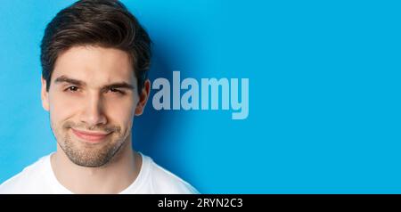 Headshot of thoughtful handsome man, looking intrigued and squinting, thinking about something, standing over blue background Stock Photo
