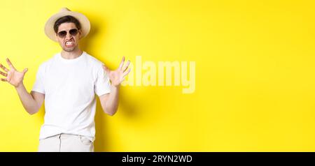 Tourism, travelling and holidays concept. Sassy young man on vacation, showing something big and clenching teeth, standing in su Stock Photo