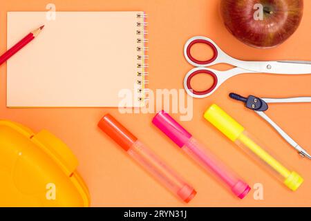 Apple, a notebook with pencil, a scissors, a compass, color felt pens and a lunch box. Stock Photo