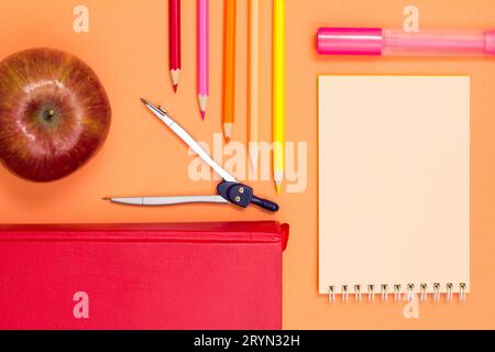 Notebook, a book, a compass, color pencils and an apple on the pink background. Stock Photo