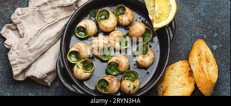 Escargots de Bourgogne Snails with Garlic Butter and Parsley in black cast iron pan with Lemon and Toasted Baguette Slices on ru Stock Photo