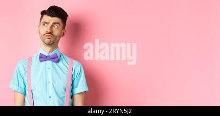 Pensive young man in romantic outfit, looking away and thinking, standing thoughtful on pink background in fancy bow-tie and shi Stock Photo