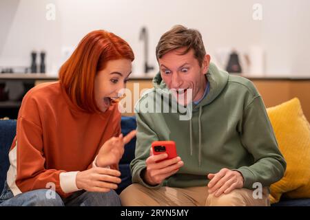Amazed shocked happy man woman rejoicing looking at smartphone screen at home. Stock Photo
