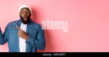 Amazed Black guy showing awesome promo offer, staring at camera excited and smiling, pointing fingers at upper left corner banne Stock Photo