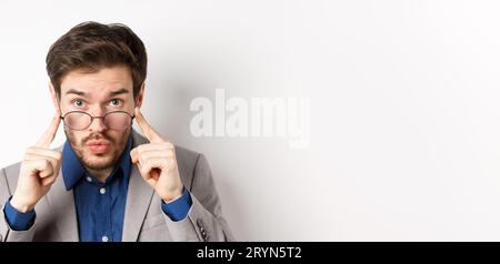 Surprised businessman takes-off glasses and look excited at camera, checking out interesting deal, standing on white background Stock Photo