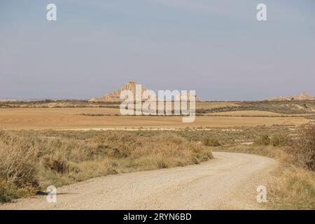 Gravel road through desert landscape of the arid plateau of the Bardenas Reales leading to bizarre rock formation, Arguedas, Navarra, Spain Stock Photo